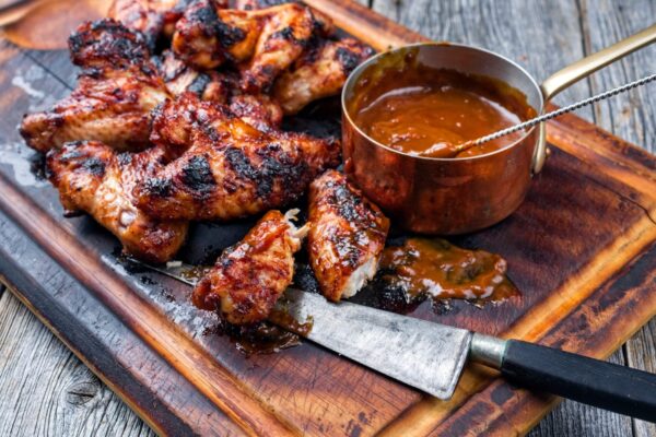 Traditional barbecue chicken wings with hot chili sauce as top view on a burnt cutting board